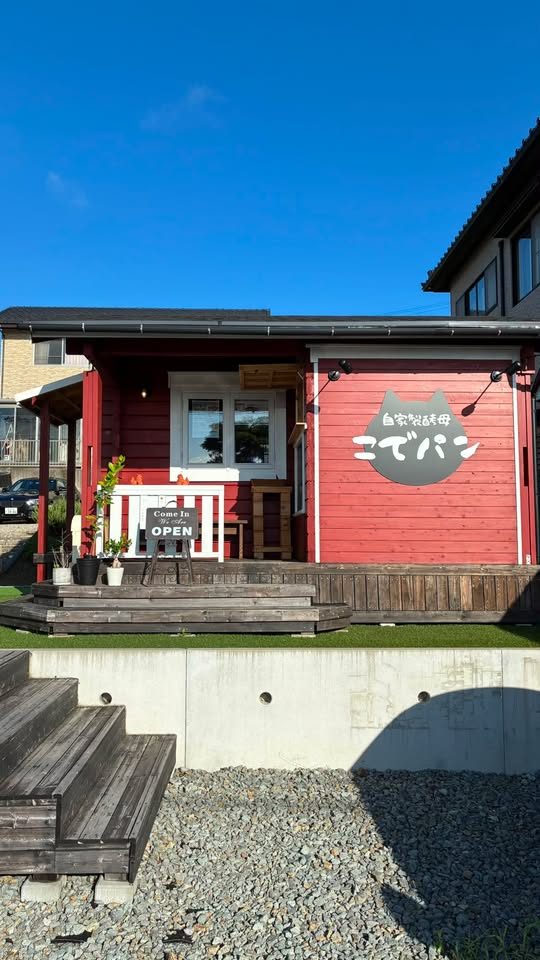 自家製酵母 こでパンの赤いログハウスの外観。ウッドデッキにOPENの看板が置かれている