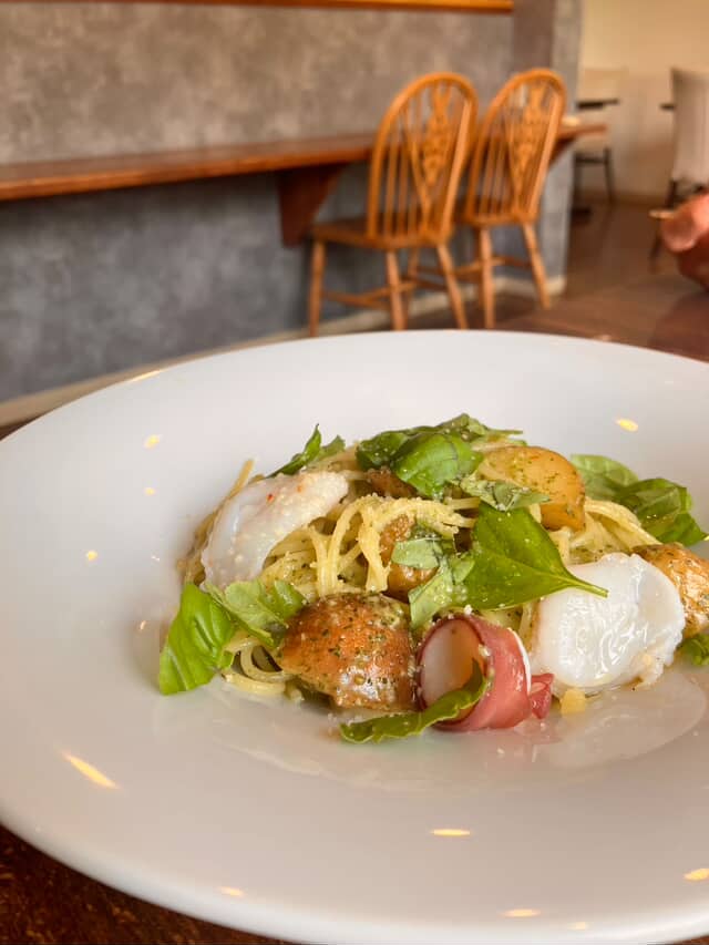 葉野菜と生ハムをあしらった、白い皿の本日のパスタ