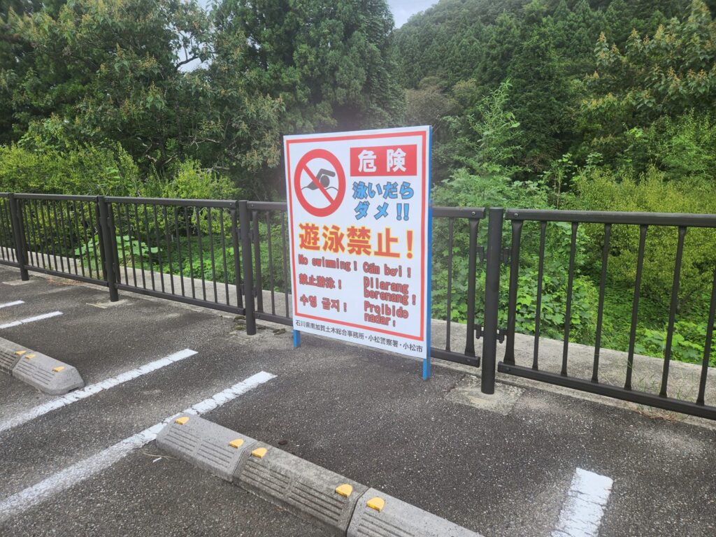 駐車場の柵に付いた遊泳禁止の看板。4か国語で書いてある